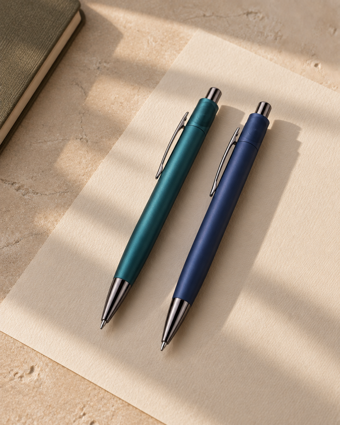 Teal and navy click pens with polished metal details on textured paper